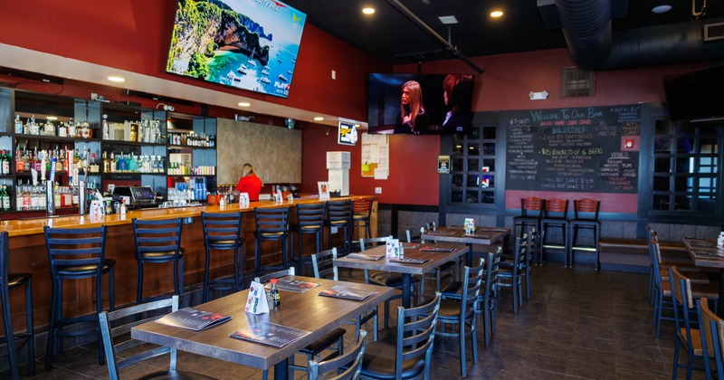 Bar area - wooden tables, a long bar counter and large TVs on red-painted walls