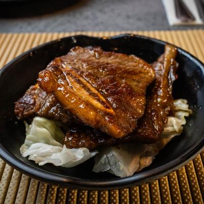 Grilled Korean BBQ beef short ribs served over cabbage leaves in a black bowl.