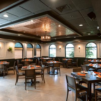 Spacious dining room with neatly set tables, large arched windows, modern lighting and greenery.
