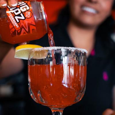 A bartender pouring strawberry margarita from a can into a glass with a salted rim and lemon.