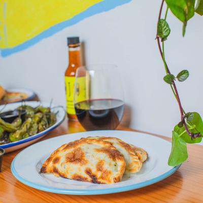 Two empanadas accompanied by red wine and shishito peppers.