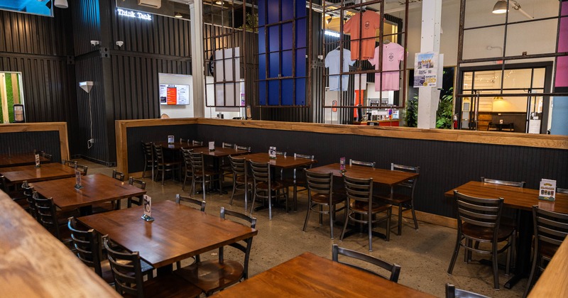Modern dining area with wooden tables, metallic chairs, and a digital menu board