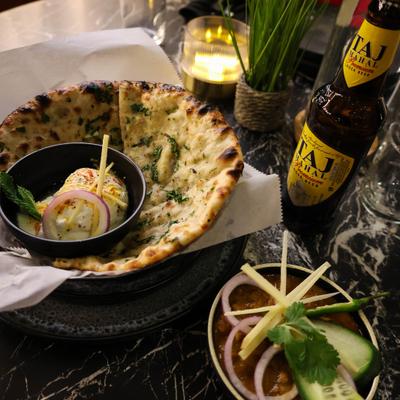 Table spread featuring naan, curry dishes and a bottle of beer.