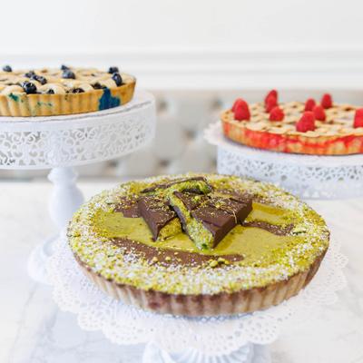 Pistachio tart with chocolate topping with blueberry and raspberry pies in the background.