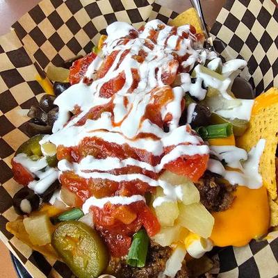 Loaded nachos served in a checkered basket, topped with salsa and drizzle of crema.