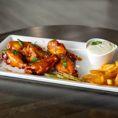 Wings coated in sauce and served with fries, pickle slices and a dipping sauce.