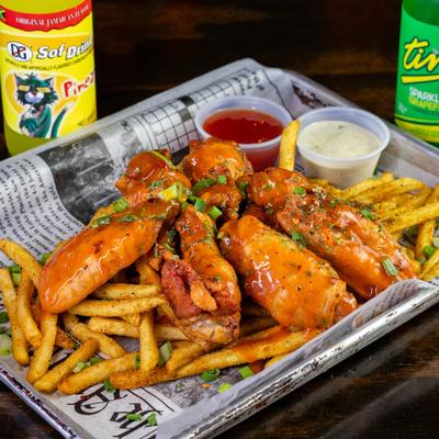 Buffalo wings served over fries with sauces on the side, accompanied with Jamaican soft drinks.