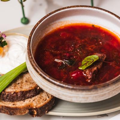 Bowl of borscht next to a plate with sour cream and two slices of rye bread.