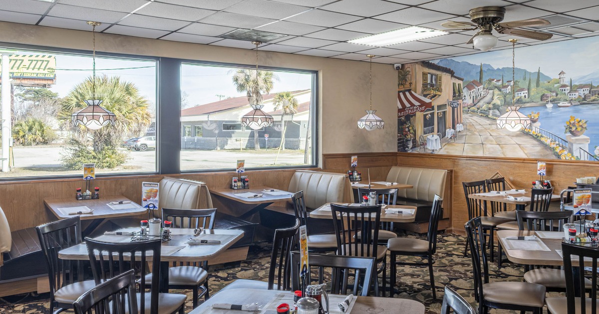 Interior of a casual restaurant with tables, chairs, large windows, and a mural
