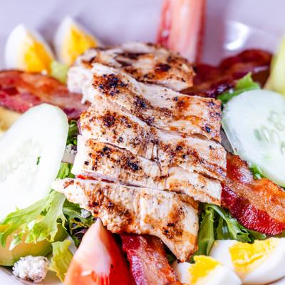 Cobb salad topped with sliced grilled chicken breast, bacon, and boiled eggs.