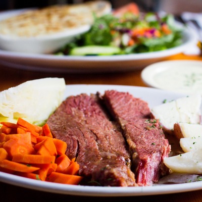 A large slab of corned beef plated next to boiled potatoes, a quarter of a cabbage and cooked carrots