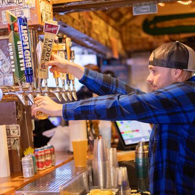 A bartender pouring a glass of draft beer from a tap.