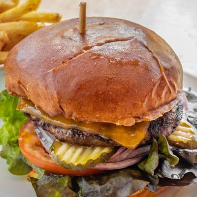 Cheeseburger with pickles and melted cheese served on a toasted bun with fries.