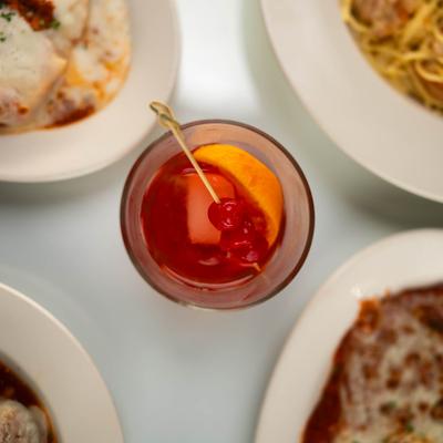 Red cocktail with orange slice and cherry garnish, overhead view.