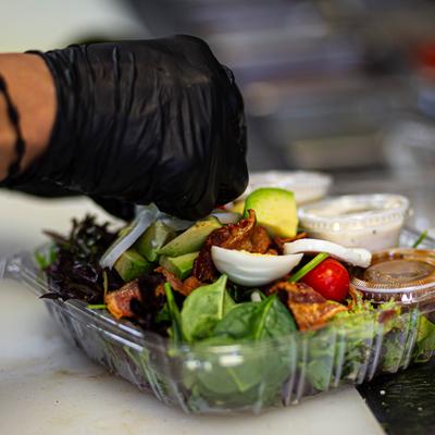 A hand in a black glove topping a Cobb salad.