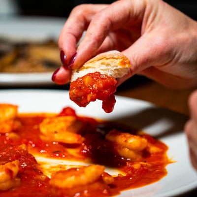 Hand dipping a piece of bread in shrimp dish with red sauce.