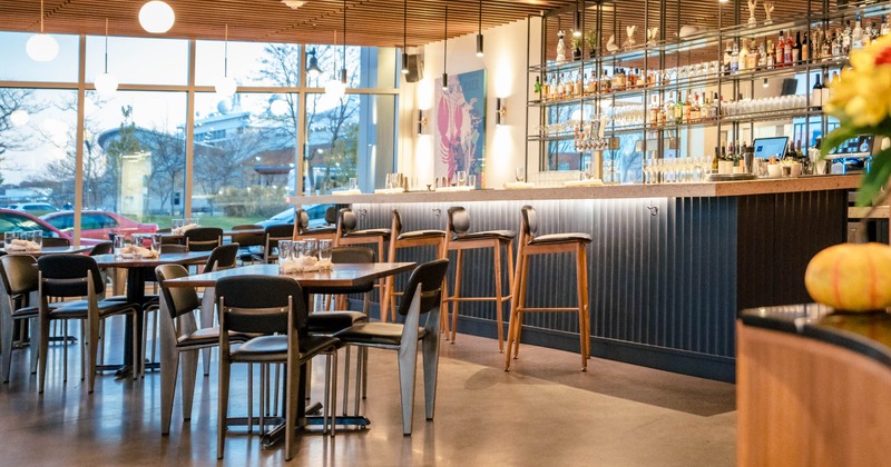 Interior of a modern restaurant with tables, a bar, and large windows