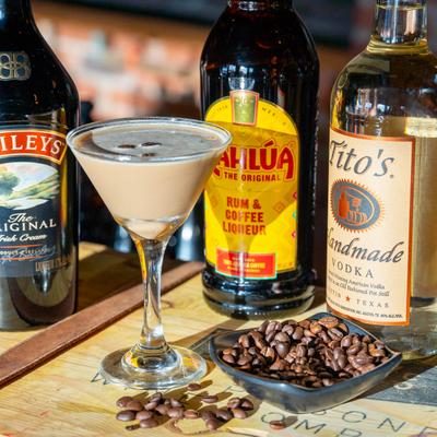 Espresso martini next to liquor bottles and coffee beans on a counter.