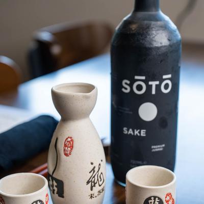 Sake bottle,  ceramic sake carafe and two cups on a wooden table.