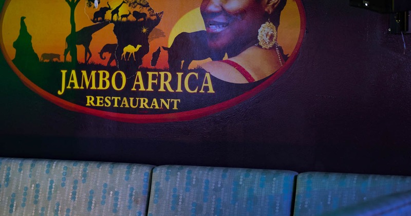 Sign of Jambo Africa Restaurant on a wall above a light blue patterned couch