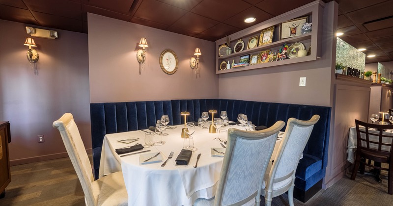 A restaurant table set for six with a blue booth and chairs surrounded by shelves with decor.