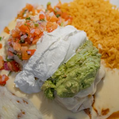 Burrito topped with guacamole, sour cream, pico de gallo, and cheese sauce with rice.