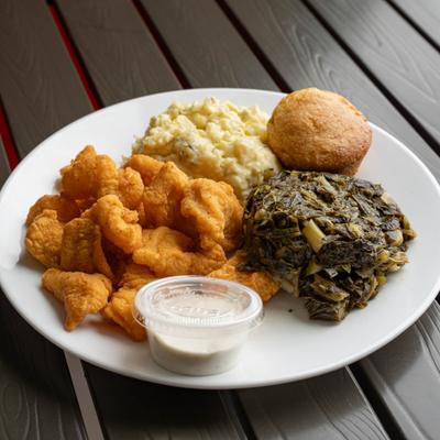 Fried fish served with sides of potato salad, collard greens and a dipping sauce.