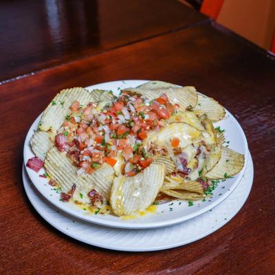 Irish nachos topped with cheese, tomatoes on white plate.