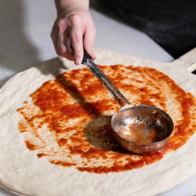 Chef applying sauce on the pizza dough.