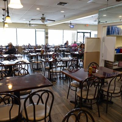 Interior with wooden tables, bentwood chairs, and large windows along the back wall.