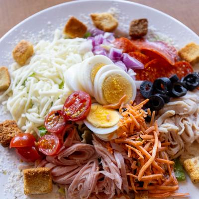 Chef salad with eggs, meats, vegetables, and shredded cheese.
