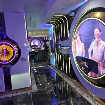 Interior, modern, neon-lit decor, circular displays featuring performers, and a polished floor.