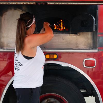A food truck worker placing a pizza into a wood-fired oven.