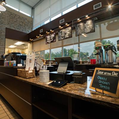 Cafe interior with a counter, stone walls, a menu board, and large windows.