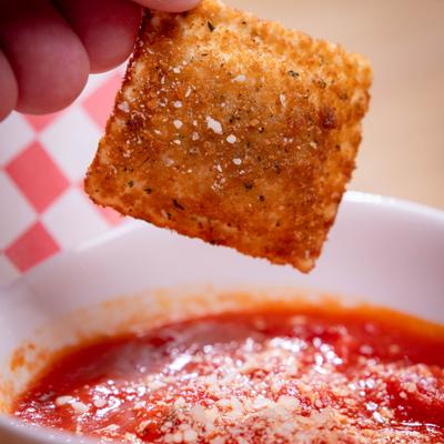 Toasted ravioli being dipped in marinara sauce.