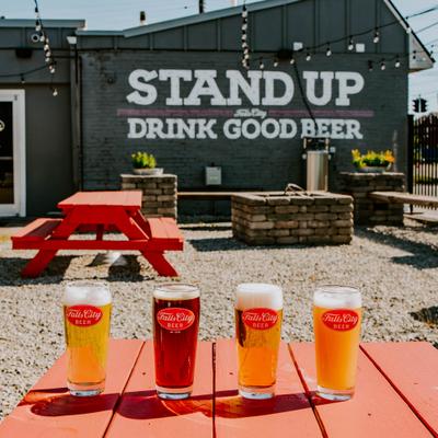 Four pint glasses of different colored beers on a red picnic table..