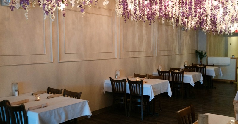 Restaurant interior with tables, hanging purple and white flowers, and soft lighting
