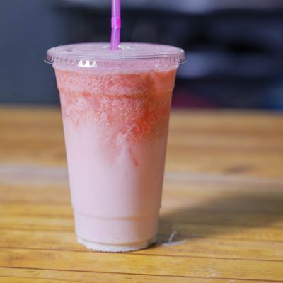 A pink smoothie with a straw on a wooden table.