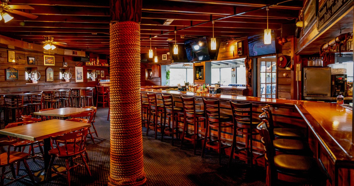 Interior of a rustic bar featuring a wooden bar counter, chairs, and rope-wrapped pillar