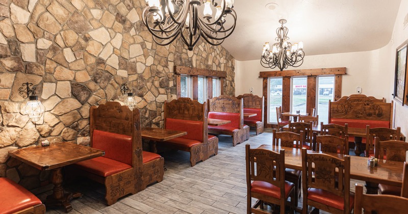Cozy interior with stone walls, wooden booths, red cushions and black chandeliers