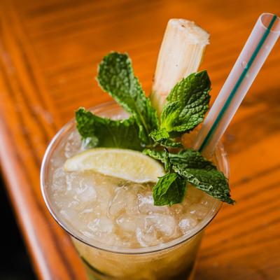 Mojito featuring a sugarcane stick, lime and mint garnish.
