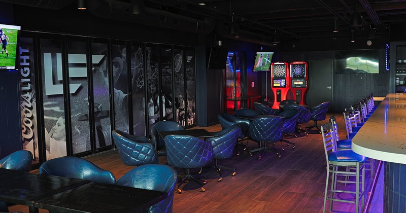 A modern bar interior - blue leather chairs, a long bar counter, dartboards, sports-themed murals