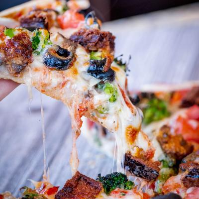 A slice of veggie pizza being lifted, showing a cheese pull and various toppings.