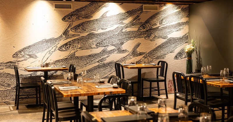 Restaurant dining room with wooden tables and black chairs in front of a large fish mural