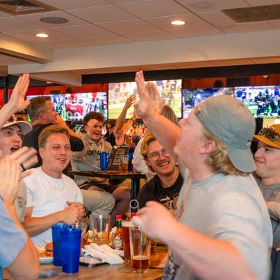 Group of patrons celebrating inside a restaurant while watching a game on TV.