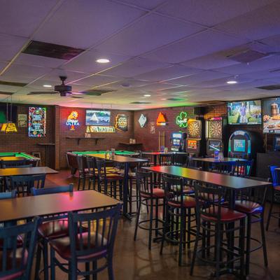 Interior with high-top seating, dartboards, and neon signs.