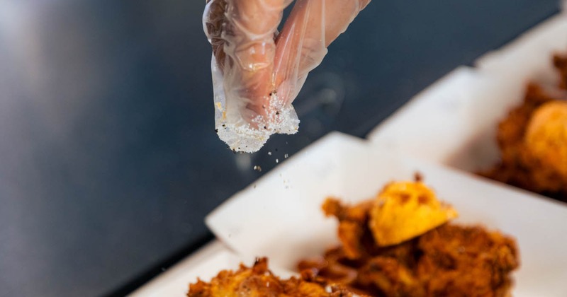 Inside the food truck, hand sprinkling seasoning on chicken and waffle serving