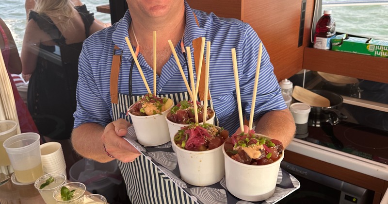 A food truck employee holding a tray with poke bowls on it