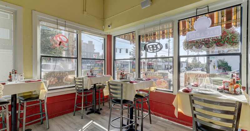 Interior with white clothed tables, tall metal chairs and large street facing windows