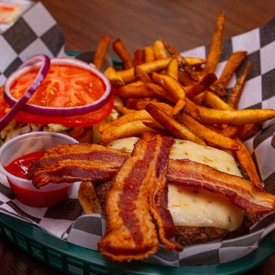 Burger topped with melted cheese and bacon, served with fries and ketchup.